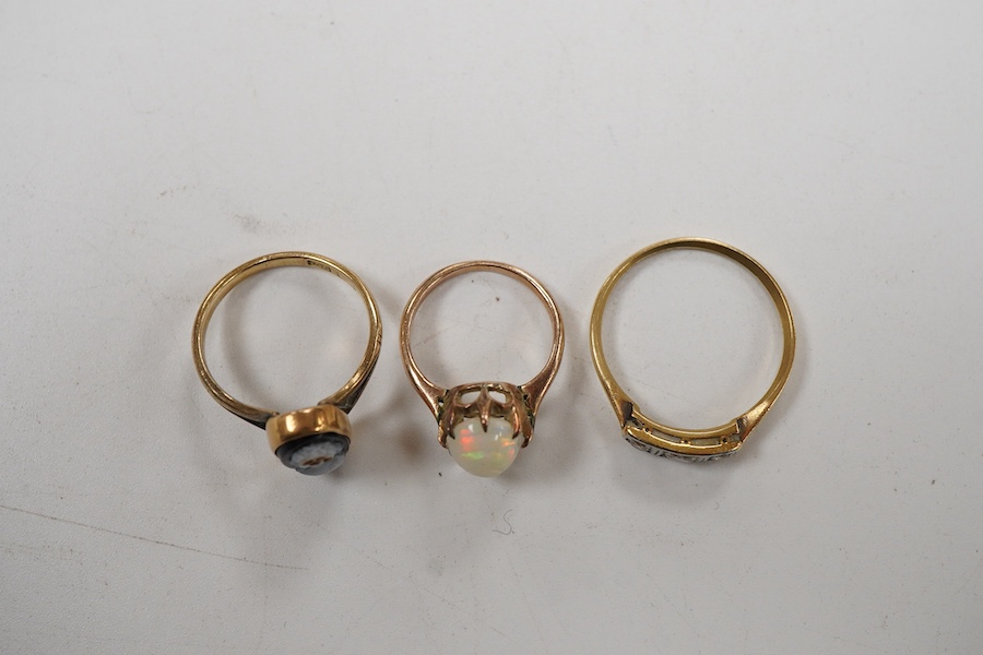 A group of rings to include a three stone diamond 18ct ring, size P, a hardstone cameo 9ct ring, size K and an opal set yellow metal ring, size D.